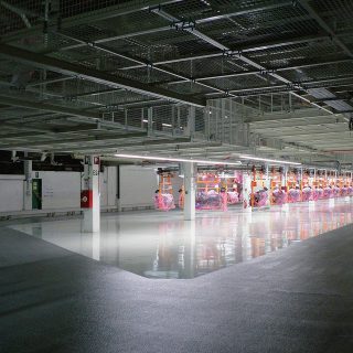 Eine unterirdische Parkgarage mit glänzendem, reflektierendem Boden, beleuchtet durch Leuchtstoffröhren, mit nummerierten Parkplätzen und sichtbarer Beschilderung.